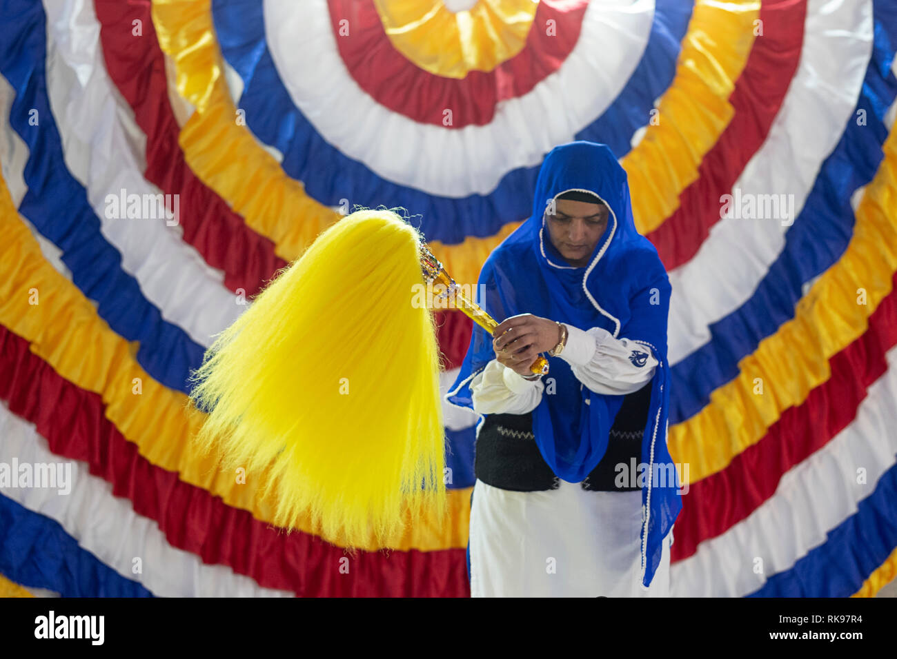 A devout Sikh woman holding a Chaur Sahib which is waving over the holy book during a morning service., At a temple in South Richmond Hill, Queens Stock Photo