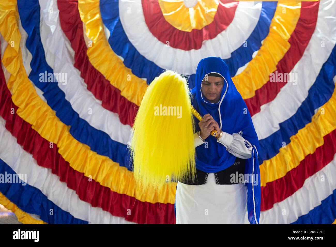 A devout Sikh woman holding a Chaur Sahib which she will wave over the holy book during a morning service., At a temple in South Richmond Hill, Queens Stock Photo