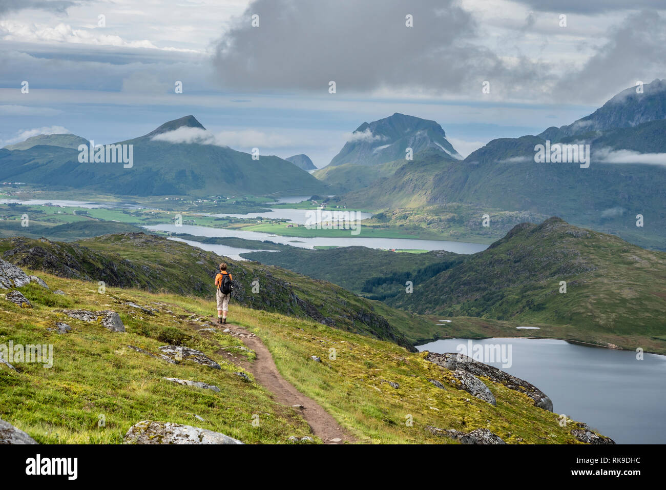 Woman on path up to mountain Justadtind, looking back to valley towards Holandsmelen and Utakleiv (mid right), Austvagöy, Lofoten, Norway Stock Photo