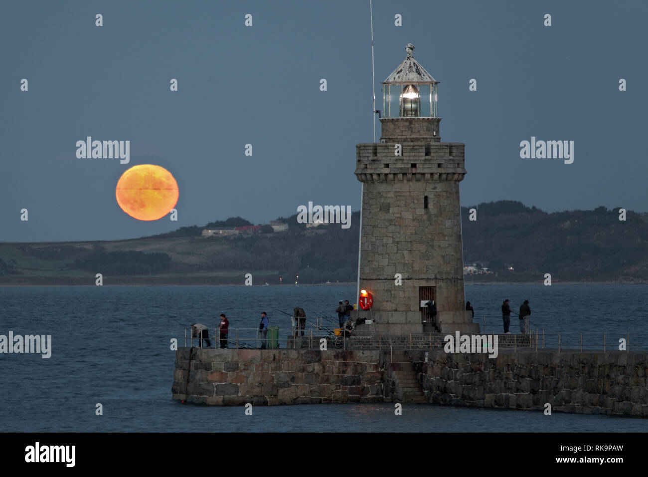 Full moon rising behind Herm Island with Guernsey breakwater lighthouse in foreground Stock Photo