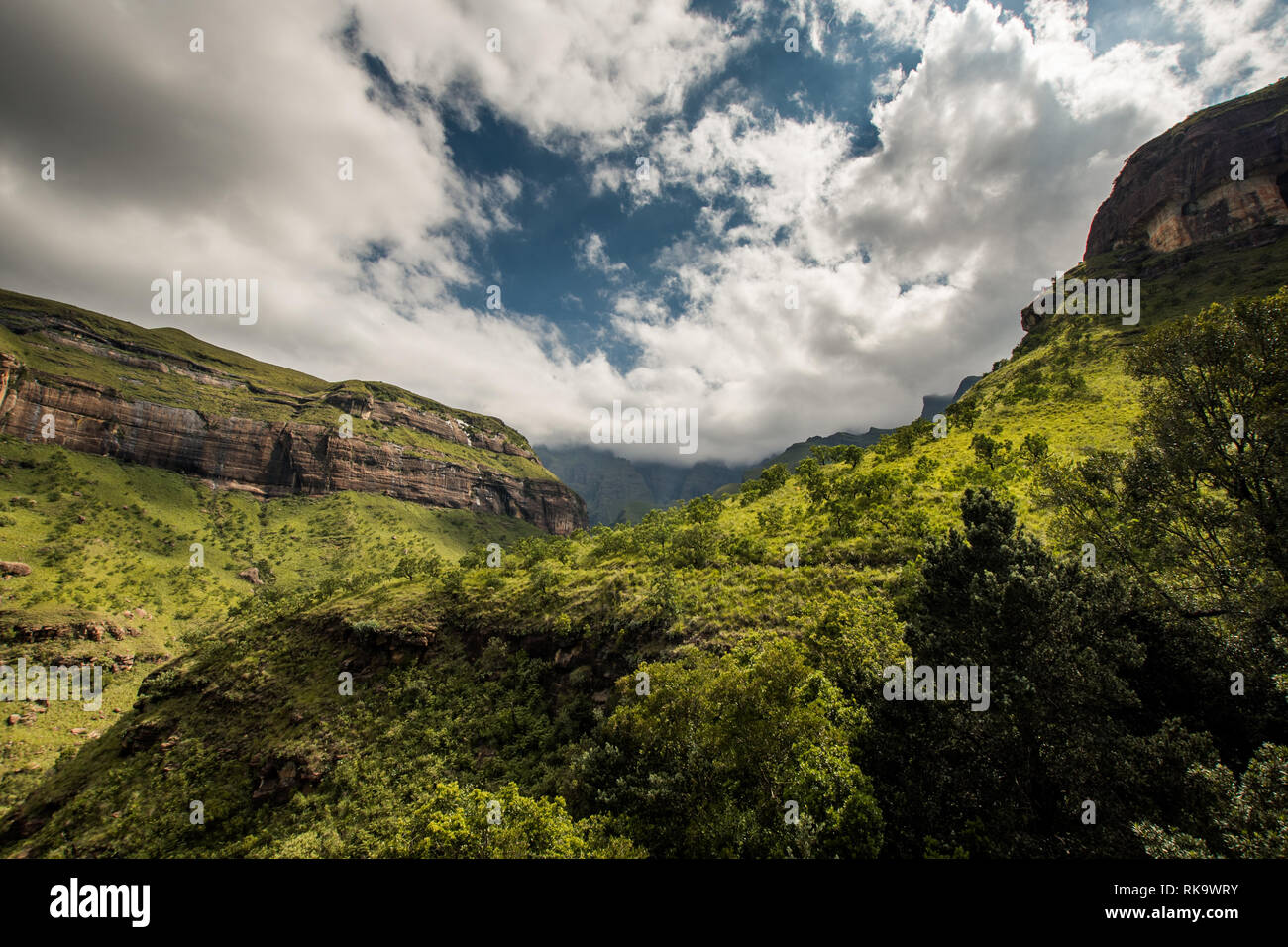 Cliffs and hillsides under a dramatic sky, along the Tugela Gorge hiking route at the base of the Amphitheatre mountain. Drakensberg, South Africa Stock Photo
