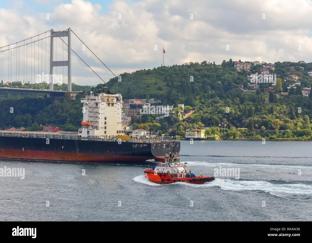 A coast guard boat escorts a large cargo ship sailing through the ...
