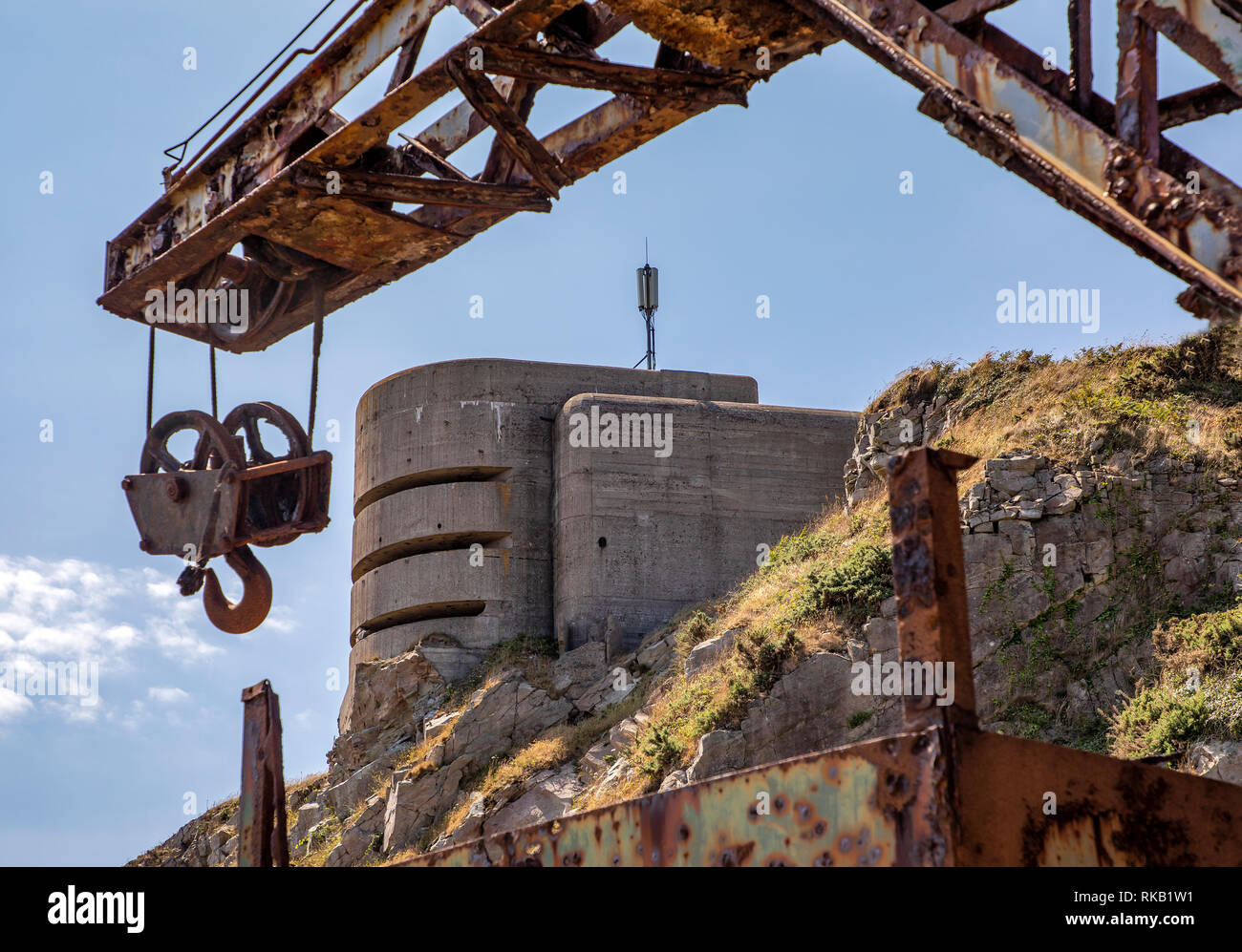 The old rail-track crane used to load stone from Mannez Quarry with the German fire control Post behind - a contrast in eras. Stock Photo