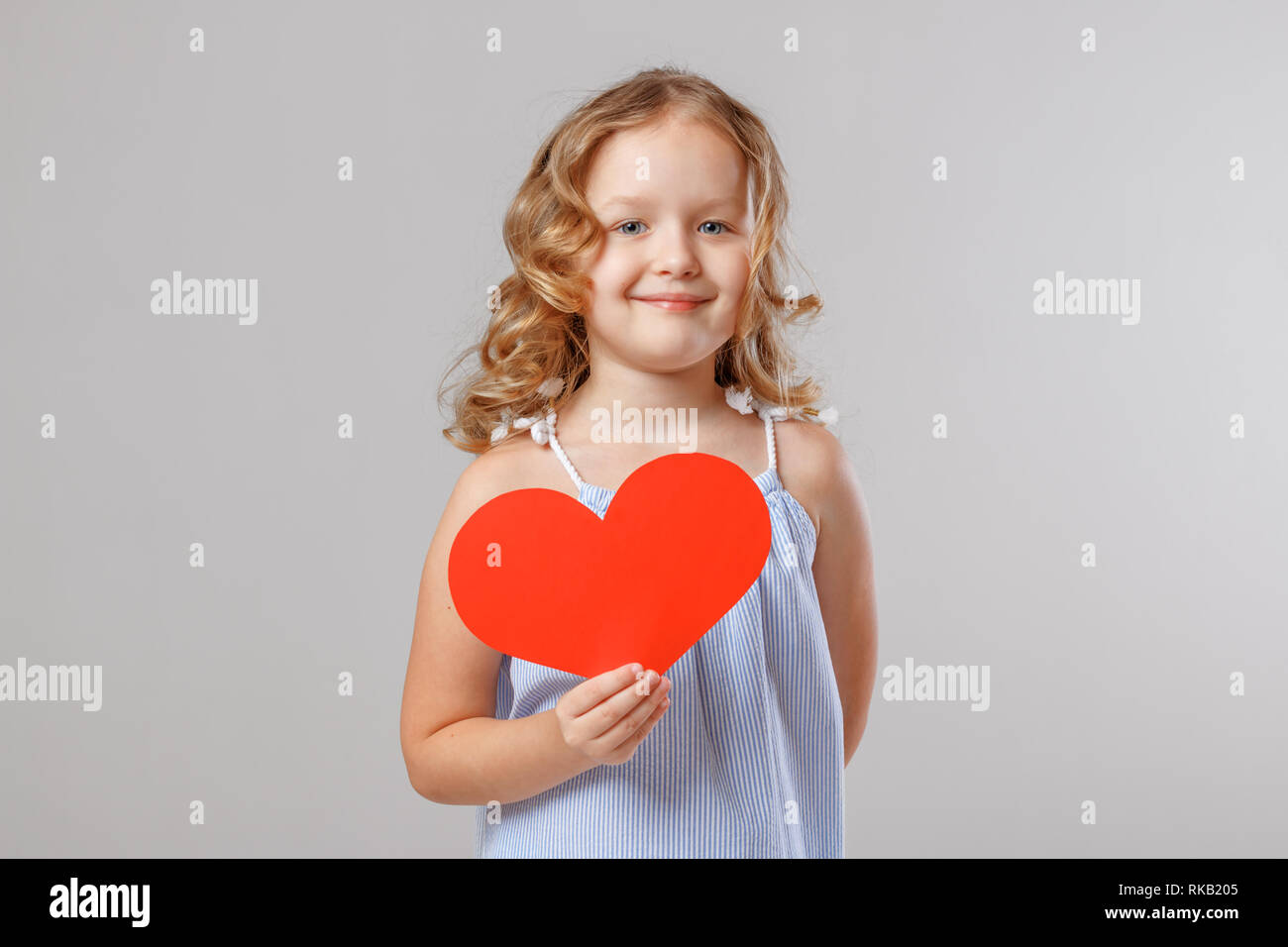 Portrait of an adorable little child girl holding a red paper heart. Gray background, studio Stock Photo