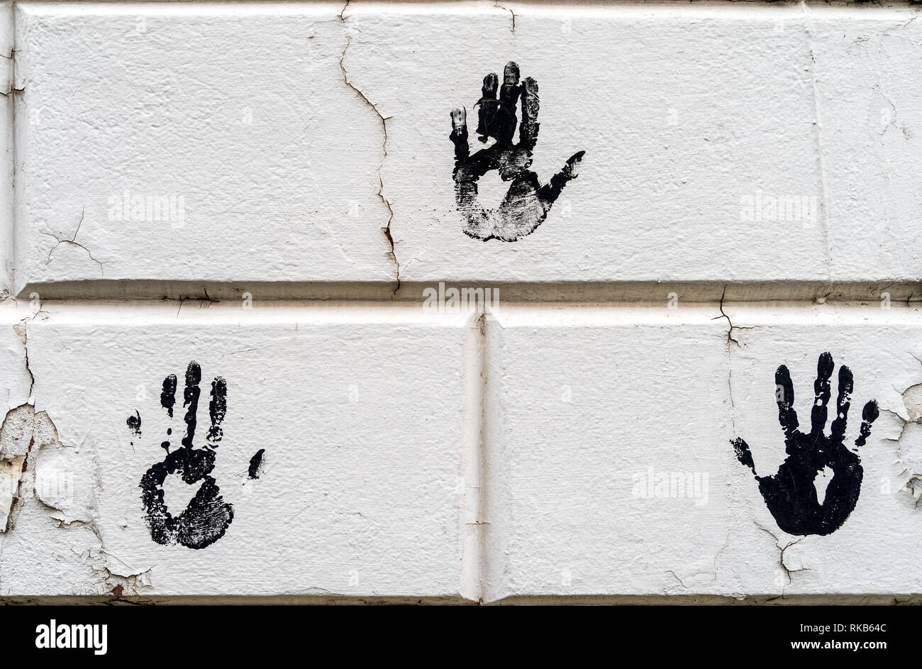 3 three black palm imprints on white large bricks with white peeling paint - high quality texture / background Stock Photo