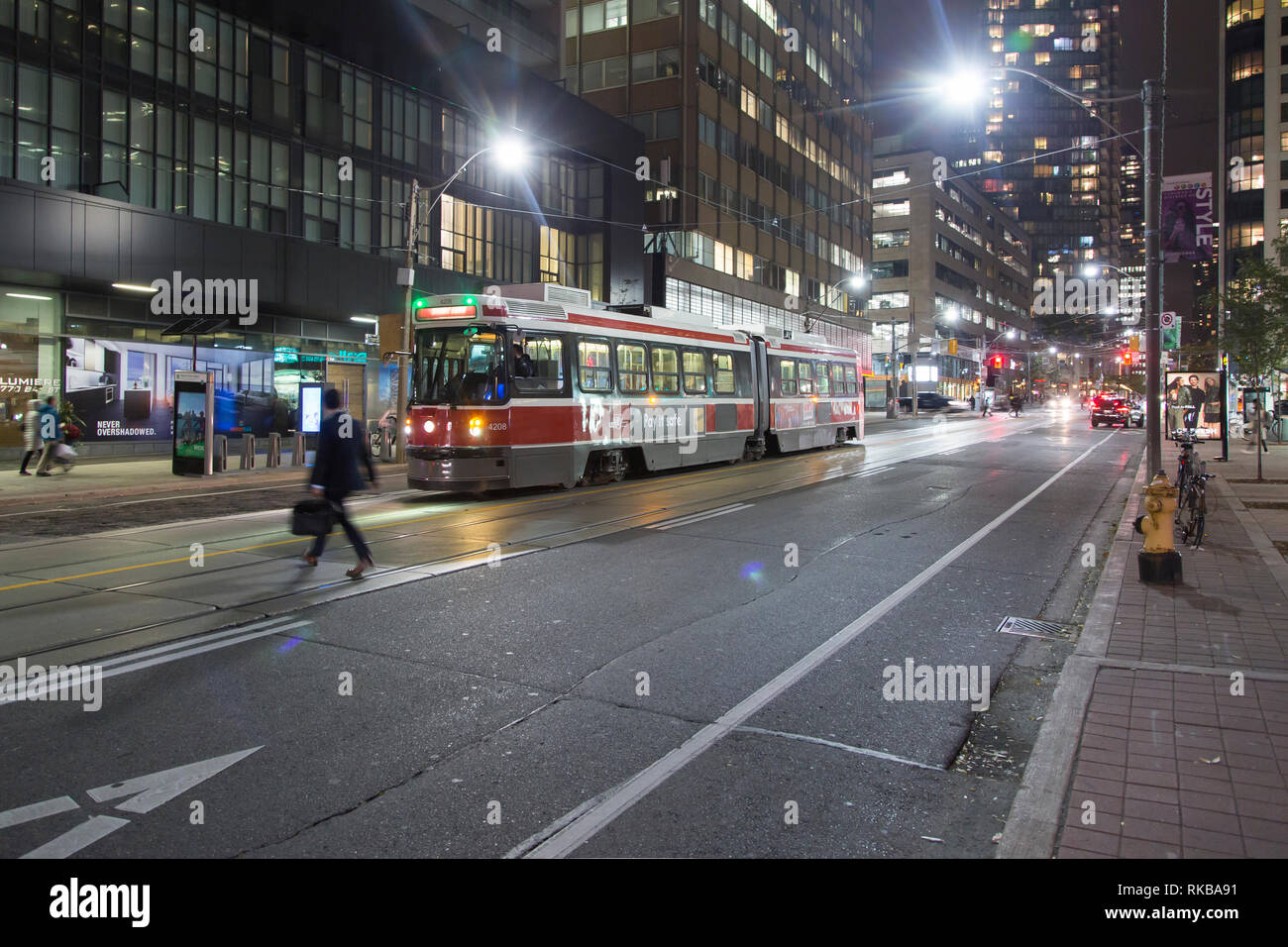 A banker crosses Bay Street as night falls on downtown Toronto. A streetcar waits on the road. Stock Photo
