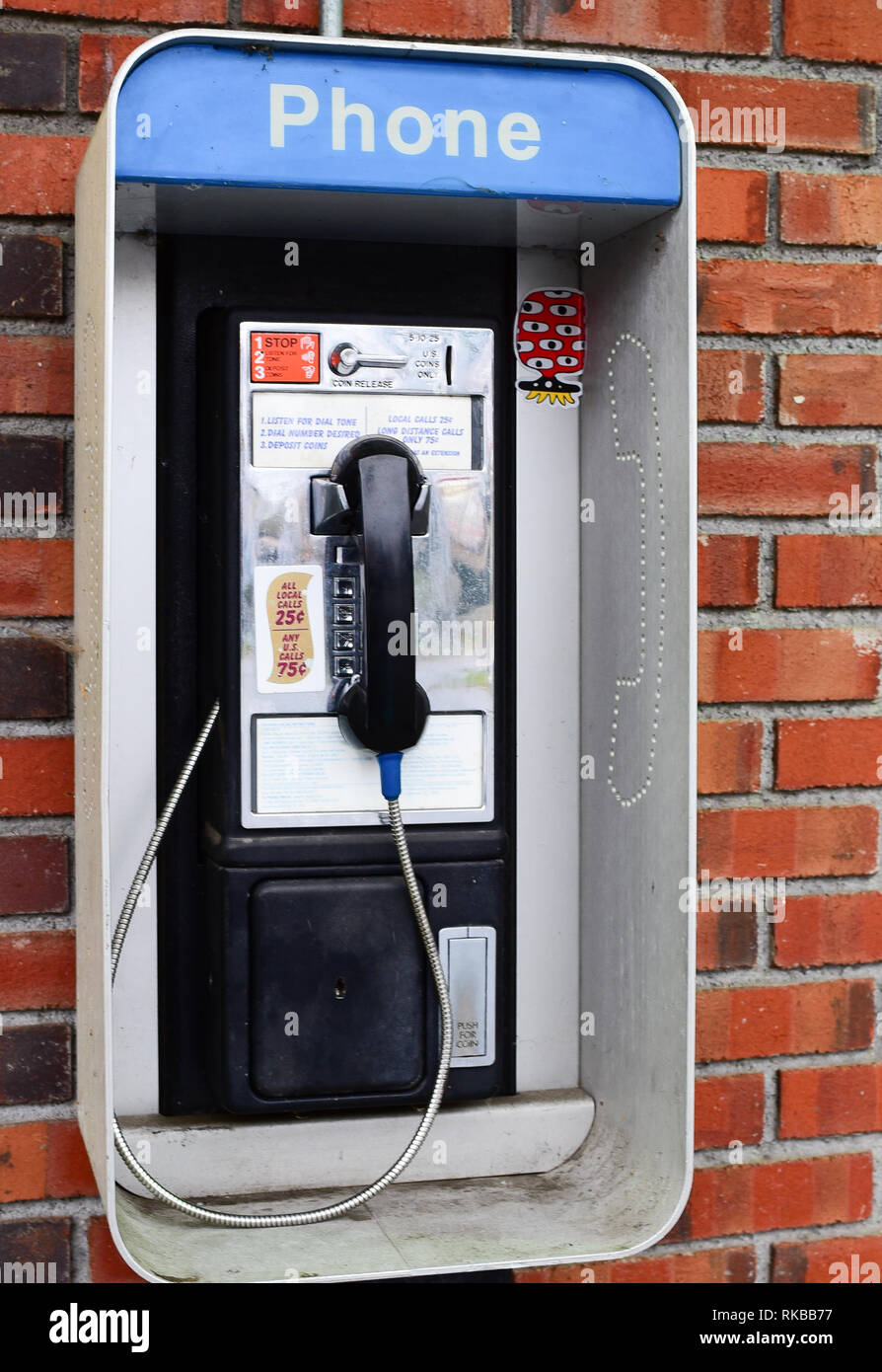 An old fashioned pay phone on a brick wall outside a convenience store in Indian Lake, NY USA Stock Photo