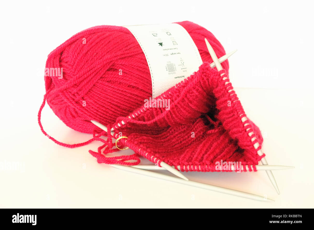 Red woollen hat being knitted on four needles on white background Stock Photo