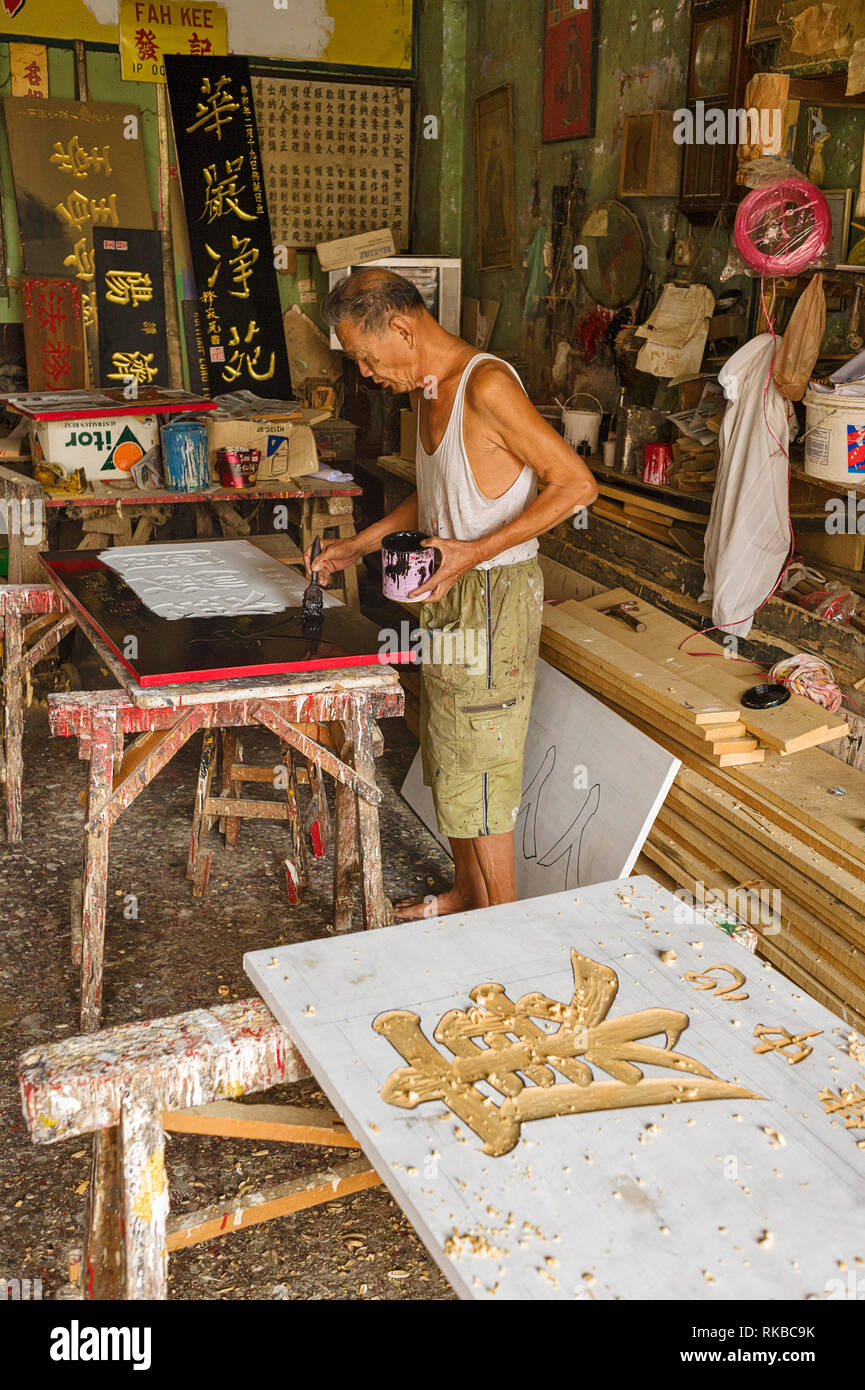 Signboard engraver carve and glid calligraphy carved on wooden panels for a Chinese store sign in Ipoh, Malaysia Stock Photo