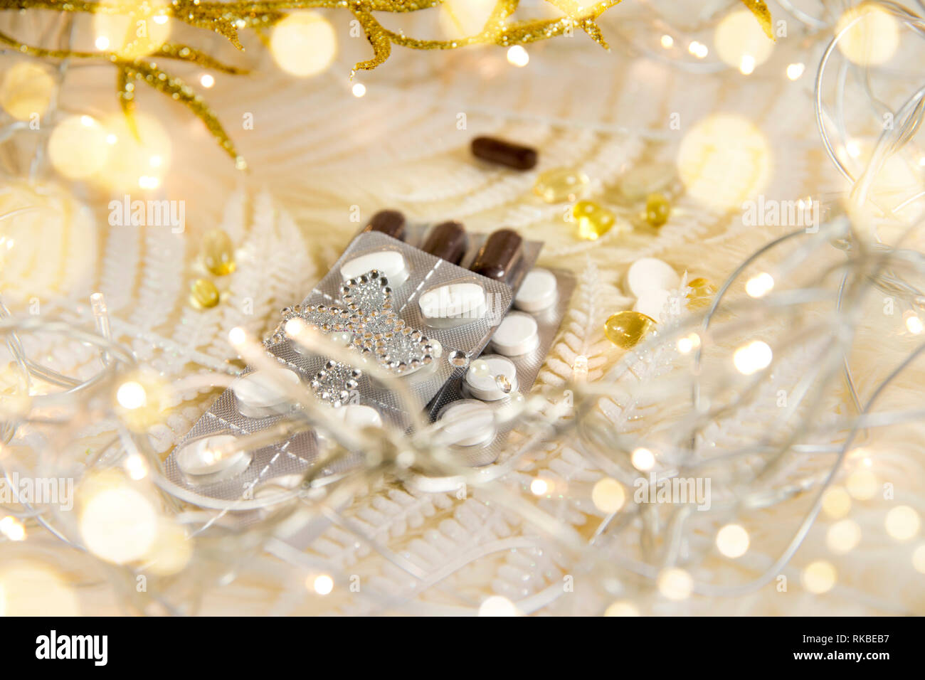 Top view of different pills vitamins as a Christmas gift idea concept on white fluffy lambskin with white decorative leaves and party lights. Recoveri Stock Photo