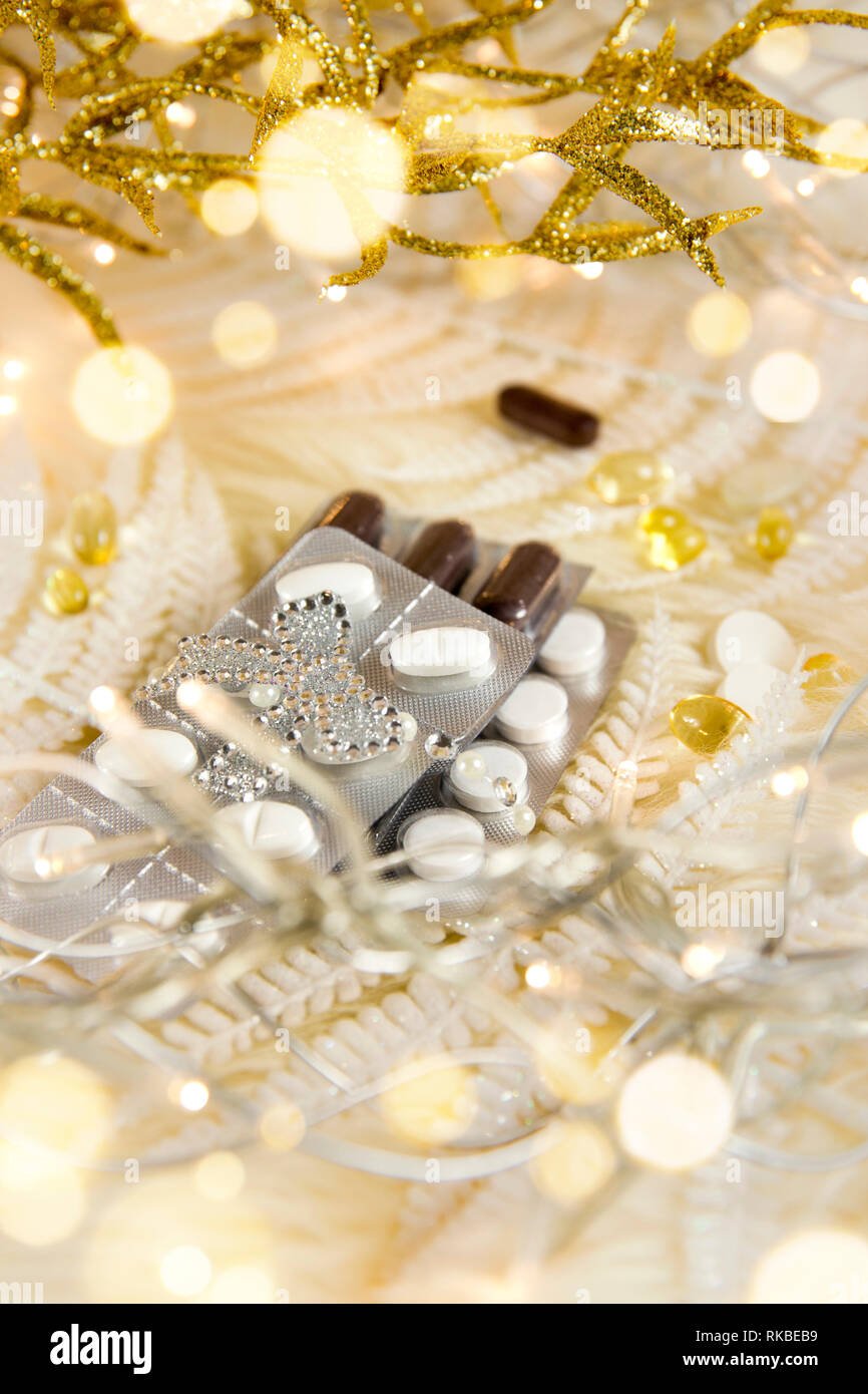 Top view of different pills vitamins as a Christmas gift idea concept on white fluffy lambskin with white decorative leaves and party lights. Recoveri Stock Photo