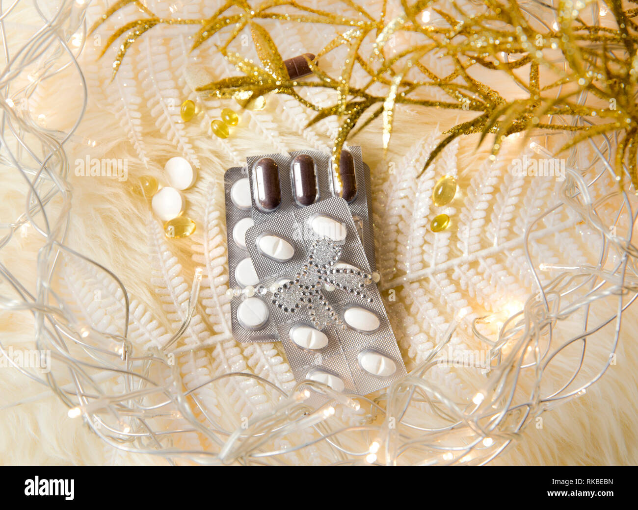 Top view of different pills vitamins as a Christmas gift idea concept on white fluffy lambskin with white decorative leaves and party lights. Recoveri Stock Photo
