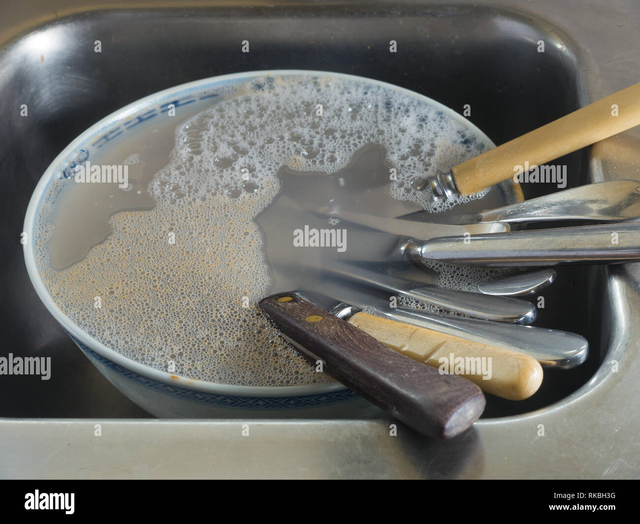 Knives in bowl filled with water and dish washing liquid  in kitchen sink. Stock Photo