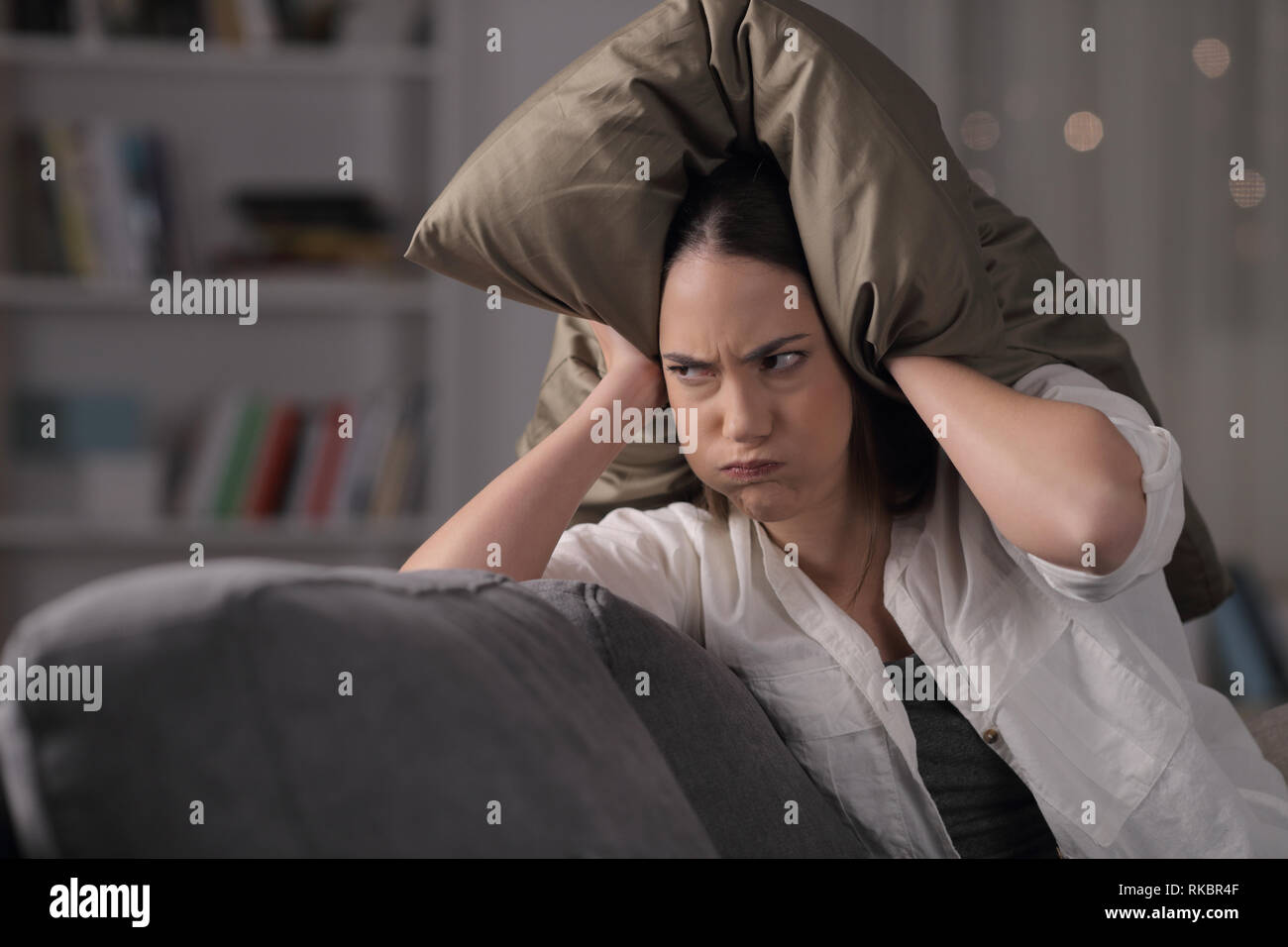 Angry homeowner suffering neighbor noise covering ears sitting on a couch in the night at home Stock Photo