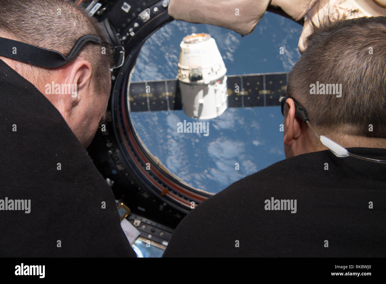NASA astronauts Scott Tingle, left, and Joe Acaba monitor the departure of the SpaceX dragon resupply spacecraft through the windows in the Cupola module aboard the International Space Station January 13, 2019 in Earth Orbit. Stock Photo