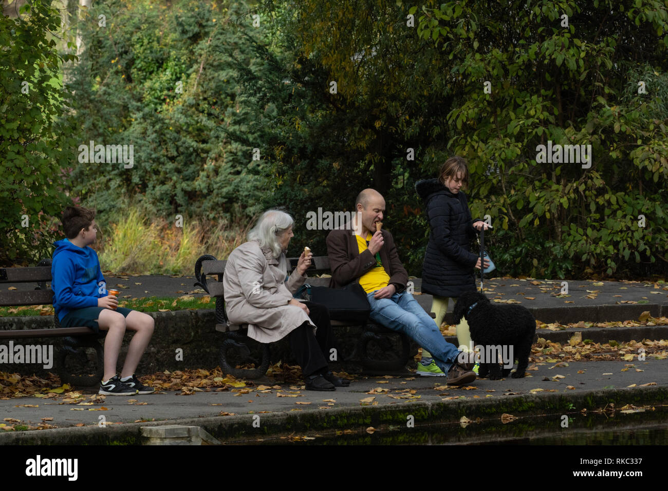 A family sat on wooden park seats and enjoying ice creams and refreshments, Valley Gardens, Harrogate, North Yorkshire, England, UK. Stock Photo