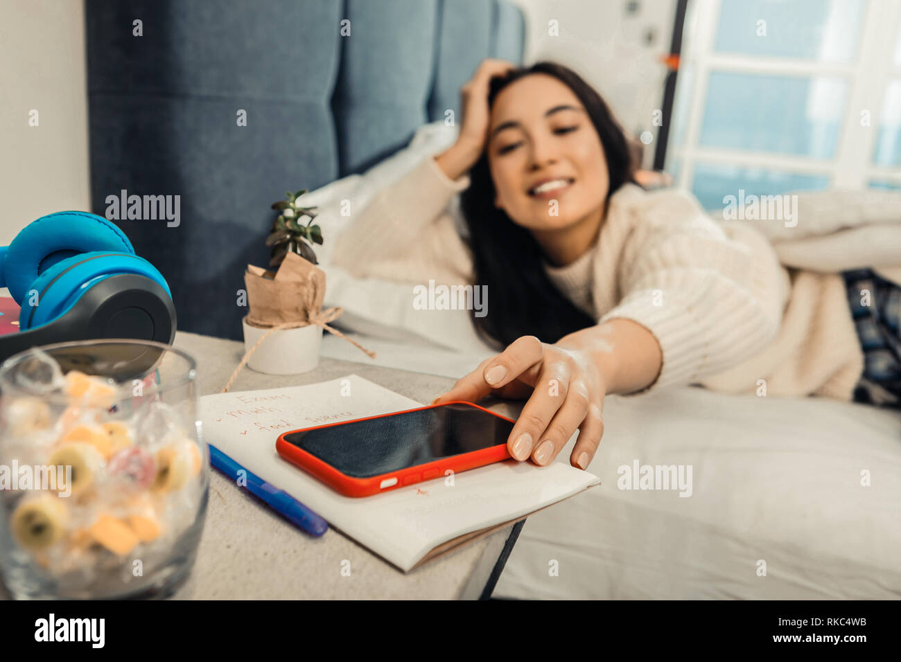 Dark-haired woman taking her red phone from the bedside cabinet Stock Photo