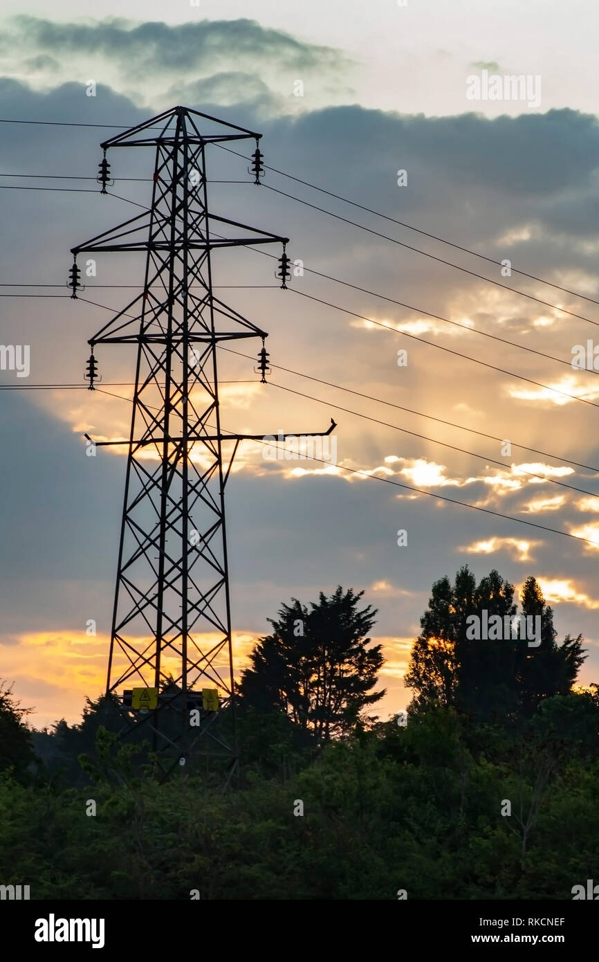 Electricity pylon with the sun rising behind creating an orange sky. Stock Photo