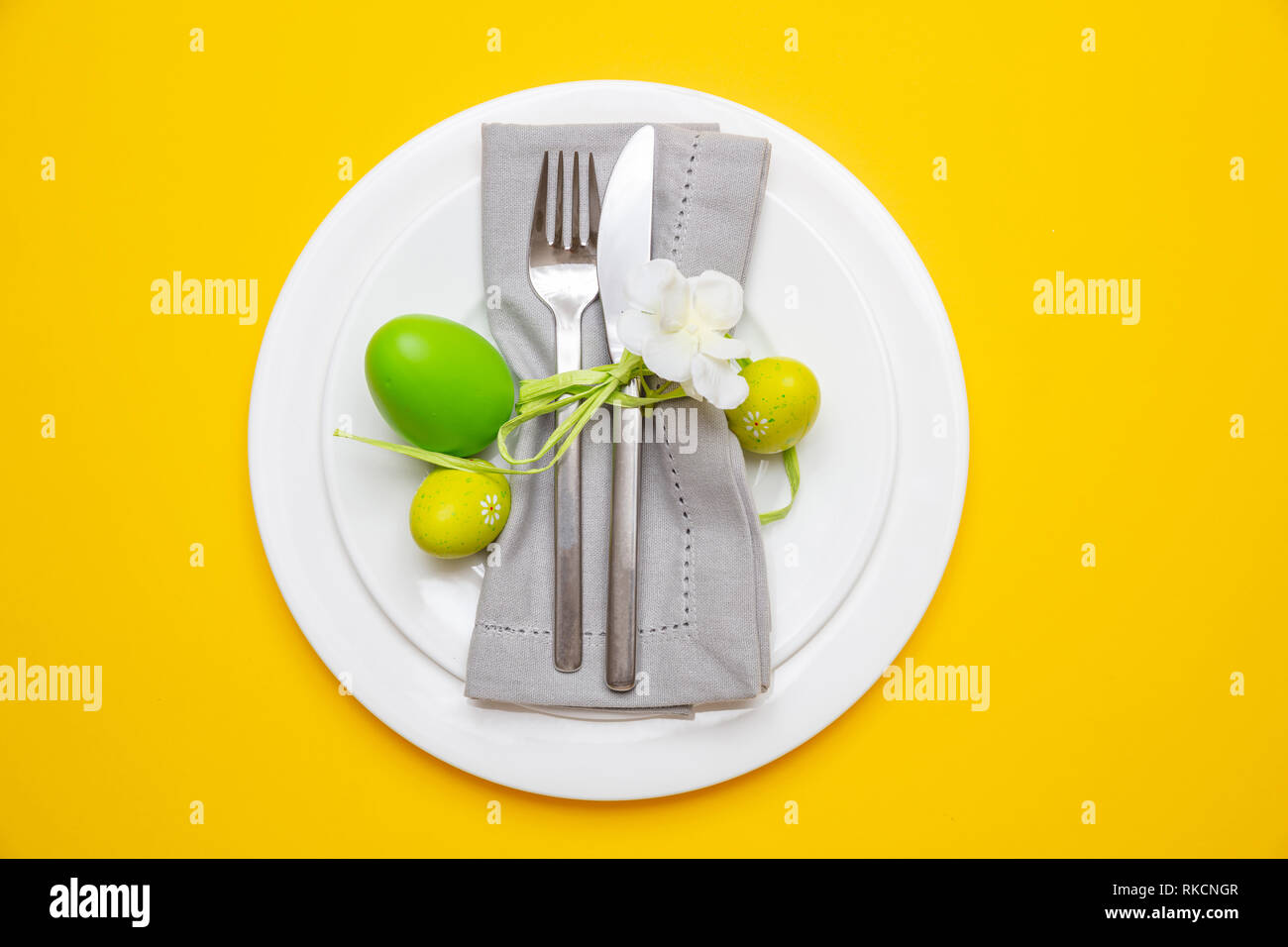 Easter table, place setting. Easter eggs, green color painted in a white plate, yellow background, top view Stock Photo