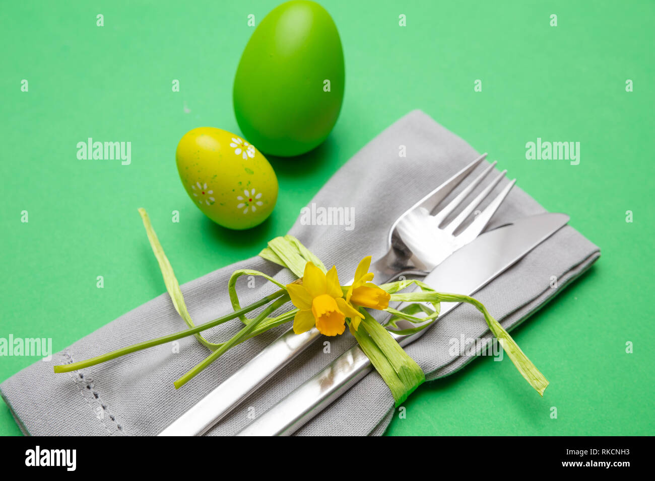 Easter table, place setting. Easter eggs, painted, cutlery and grey napkin, green color background, close up view Stock Photo
