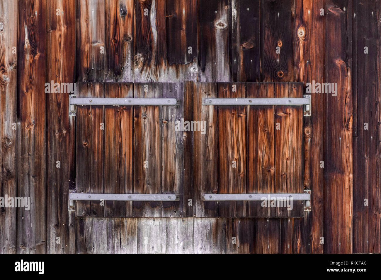 Closed window shutter of wood in a wood panel wall of alpine outbuilding with distinctive metal hinges Stock Photo