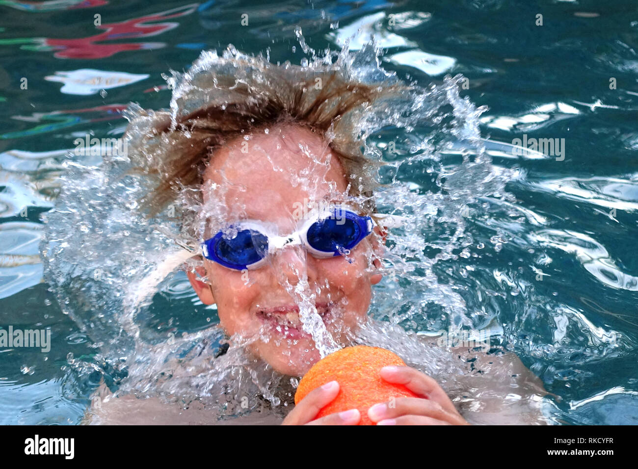 Anyoung boy gets splashed in the face with pool water coming out of a floatable noodle. Stock Photo