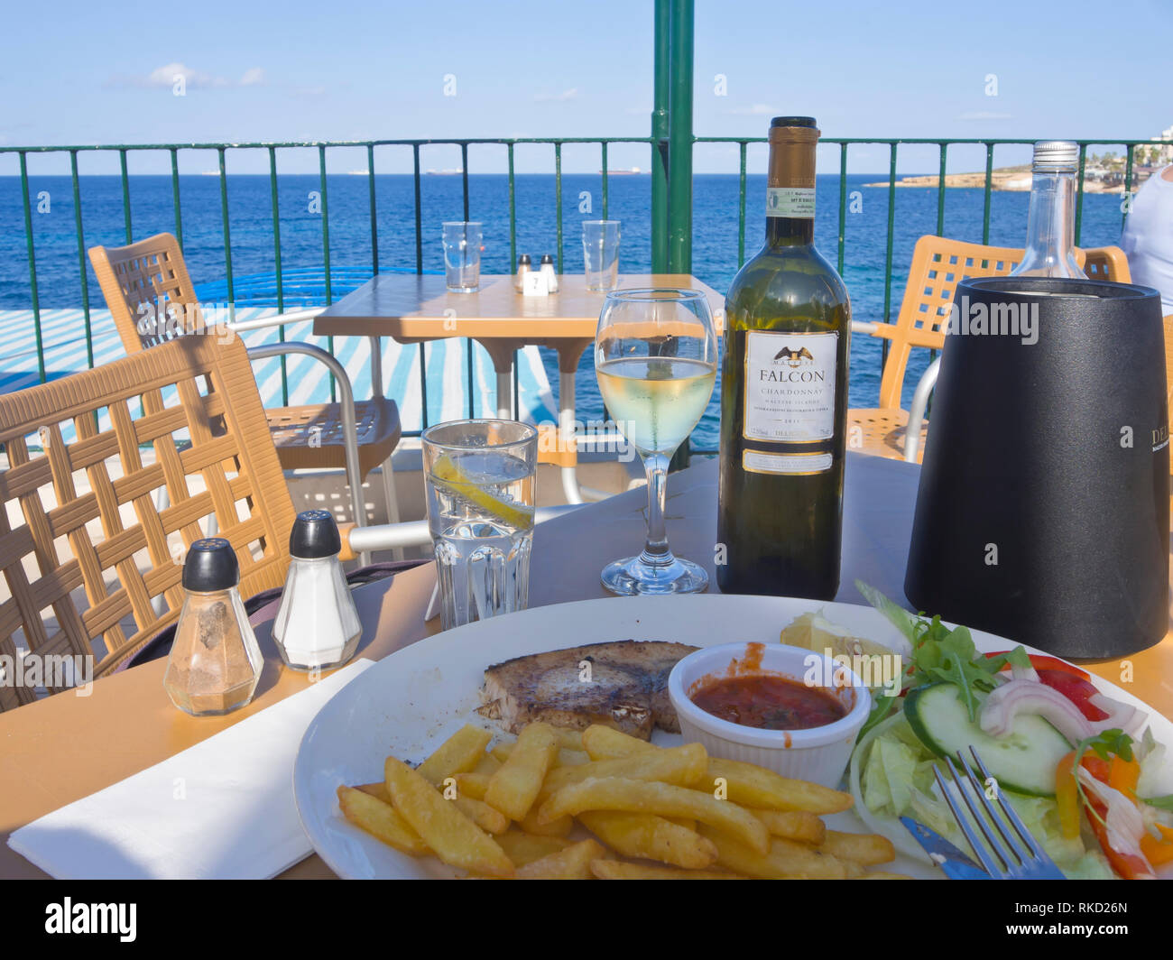 Swordfish with chips and salad and a bottle of the Maltese white wine Falcon, views of the Mediterranean sea in Bugibba St. Paul's Bay Malta Stock Photo