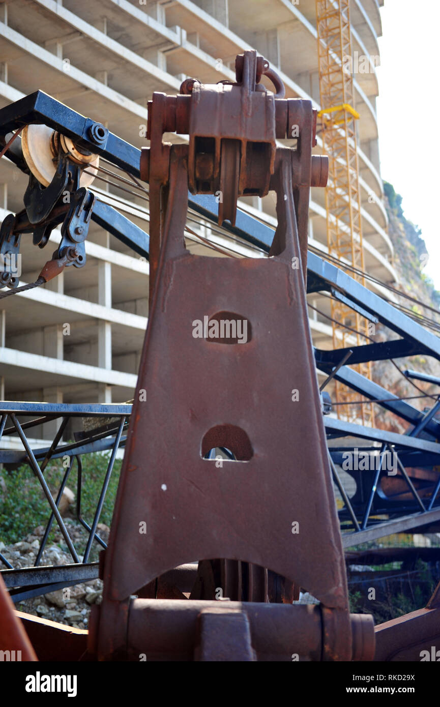 Vertical closeup of crane in front of abandoned hotel in Montengro.  Unfinished building with rusty machine in front. Stock Photo
