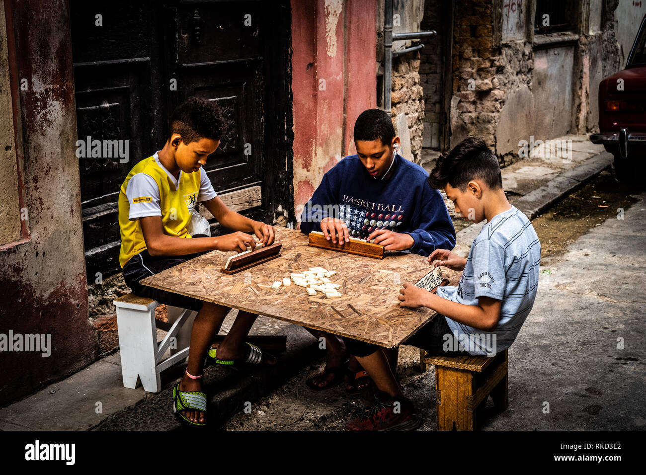 Three kids playing a board game on a wooden plate in the streets of Havana, Cuba. Stock Photo
