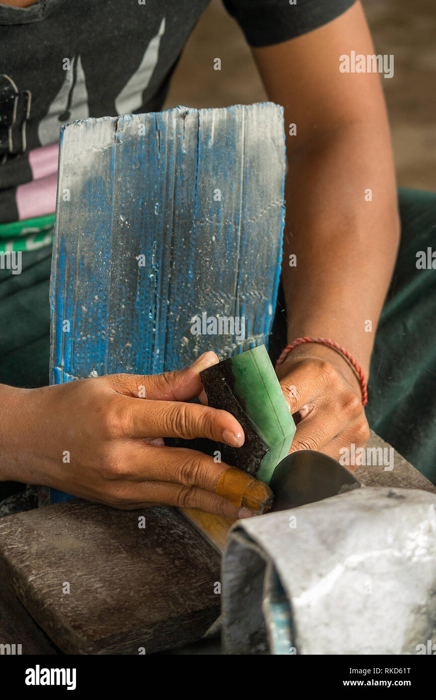 A stone worker cuts a large precious green jade stone in half, Jade Market, Mandalay, Myanmar. Stock Photo