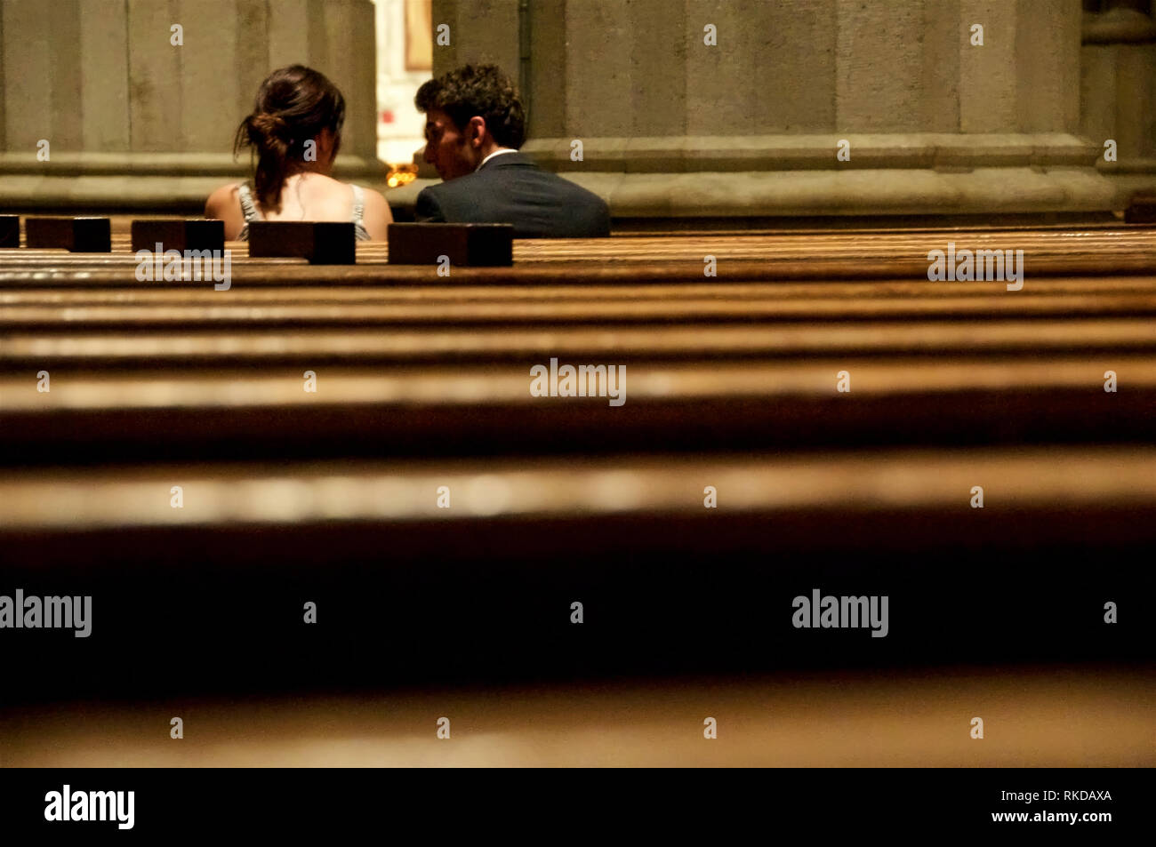 A man and a woman huddled and engaging in a hushed conversation between church pews. Stock Photo