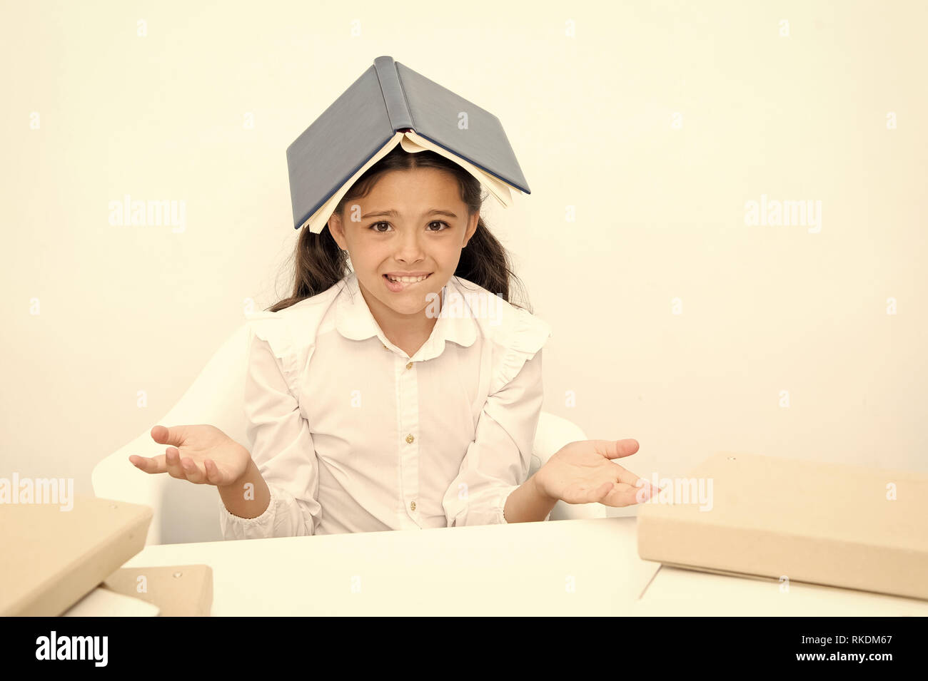 How is it possible to learn. Girl child confused exhausted with book roof on head white background. Schoolgirl tired of studying and reading. Kid school uniform tired face not want continue reading. Stock Photo