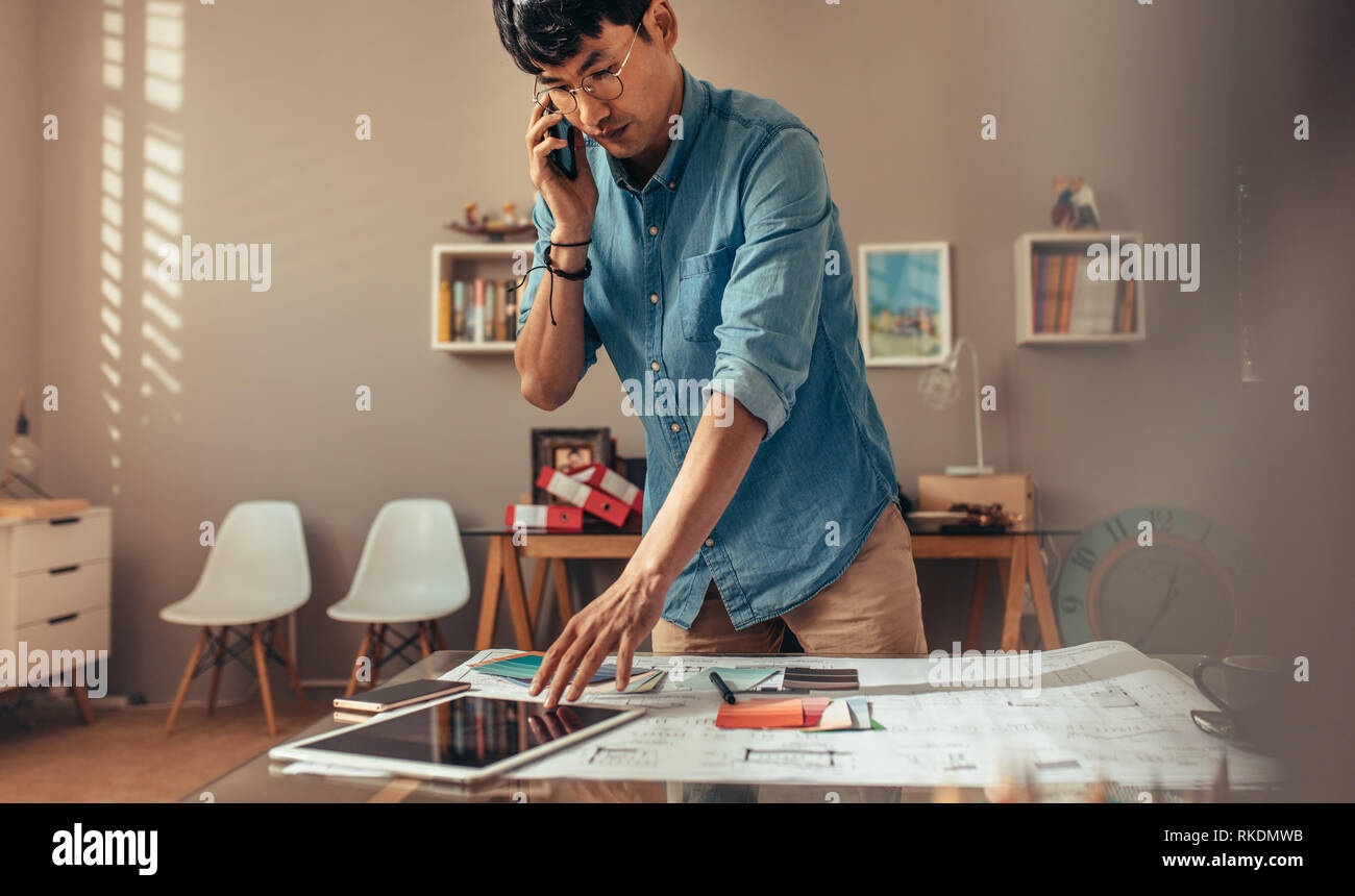 Architect talking with client over mobile phone while working at his desk. Creative professional answering phone call with working on digital tablet a Stock Photo