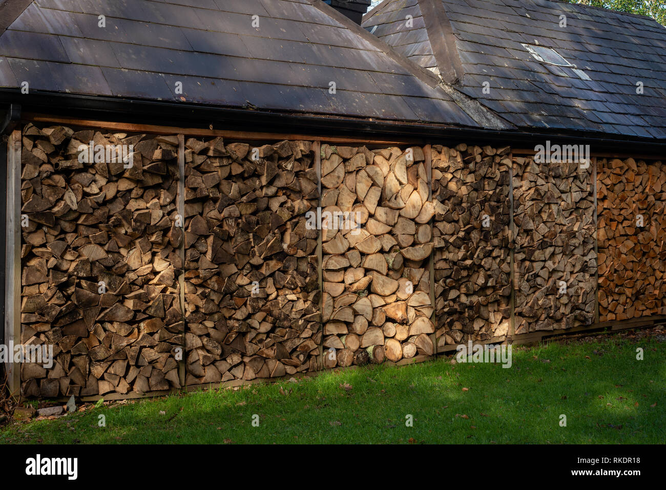 Pile of firewood cut tree logs. Stack of wood as firewood material by barn wall as home self sufficient energy in rural Ireland. Stock Photo