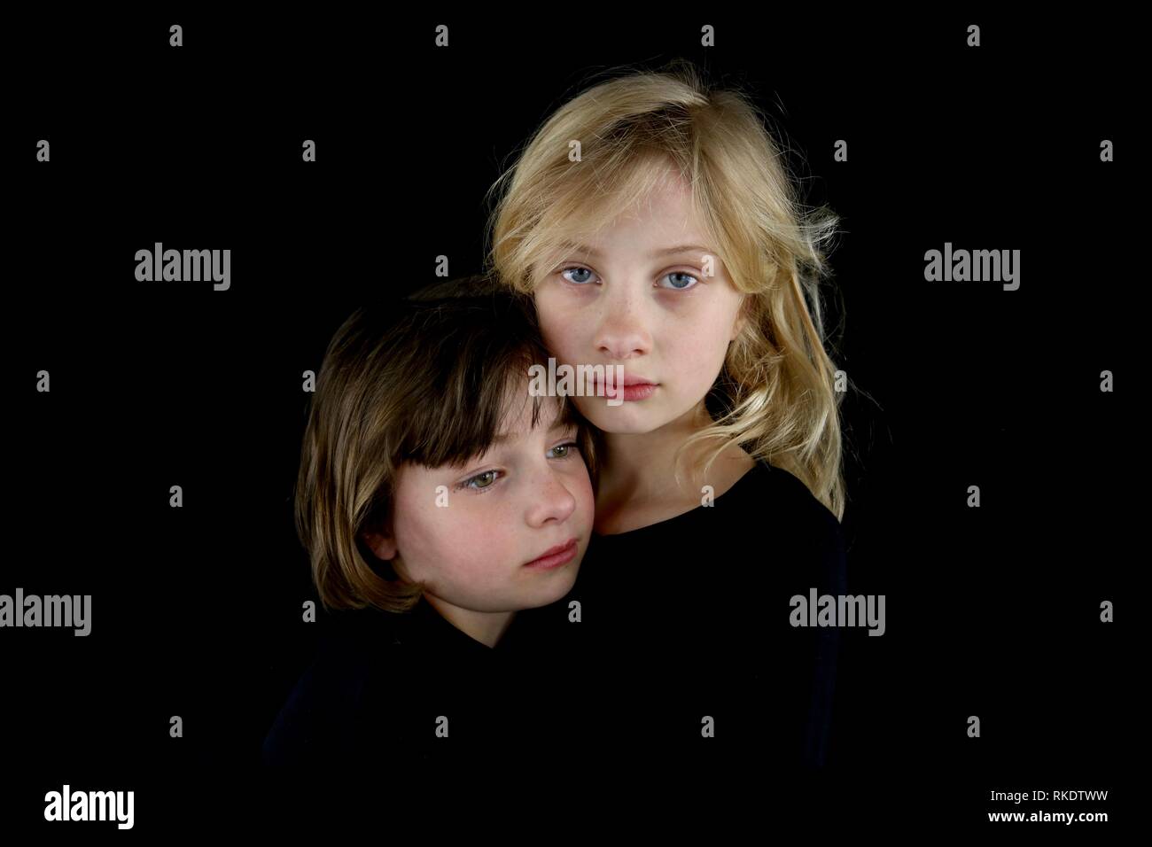 Closeup of two young sisters grieving and holding each other against a black background Stock Photo