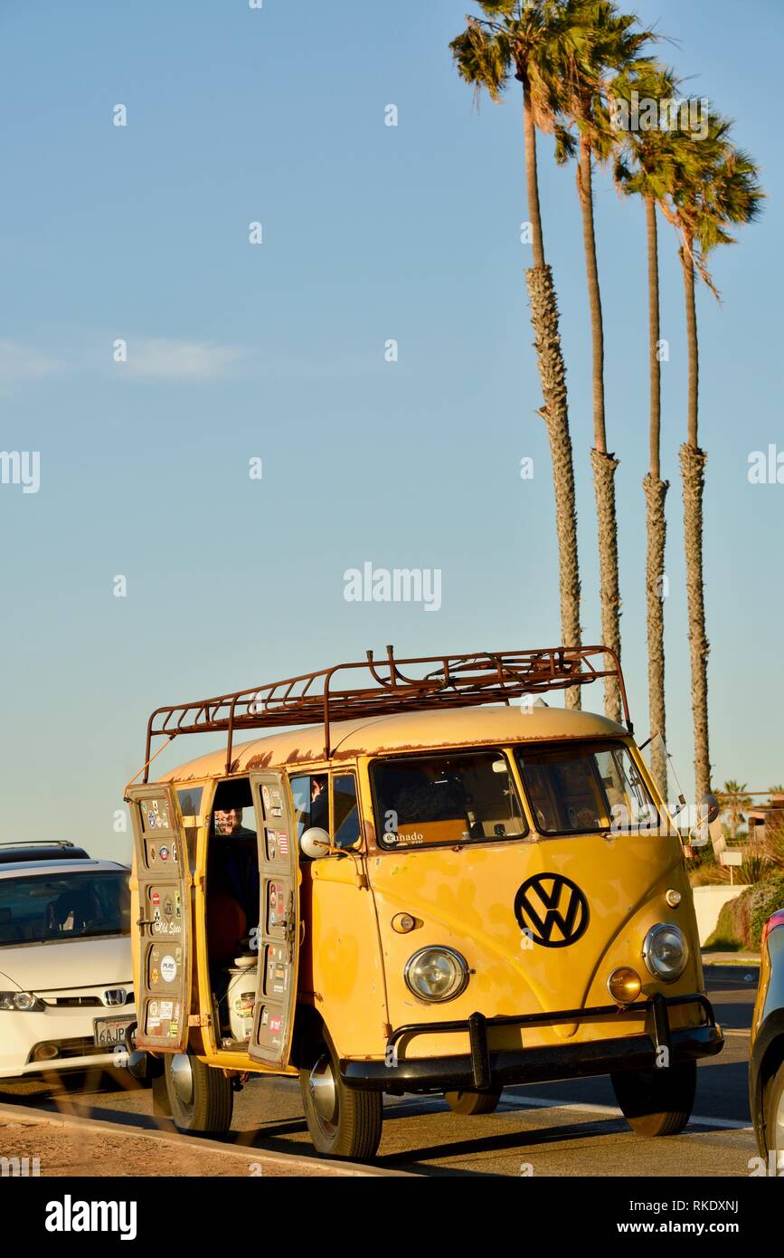 Classic 1960s yellow Volkswagon VW minibus camper van parked at Sunset Cliffs at sunset, doors open with palm trees, San Diego, USA Stock Photo