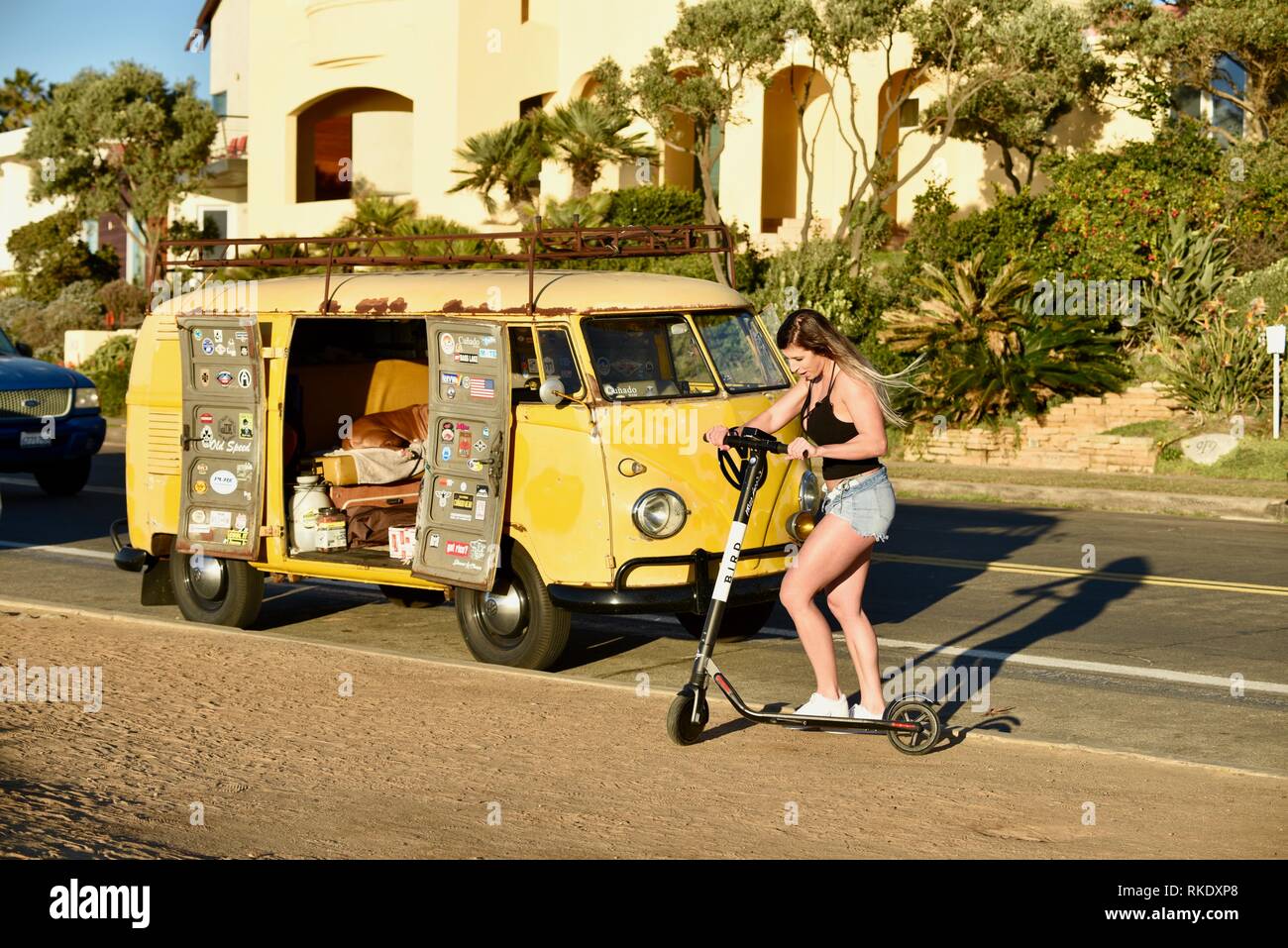 Attractive young woman hopping on Bird electric scooter next to classic