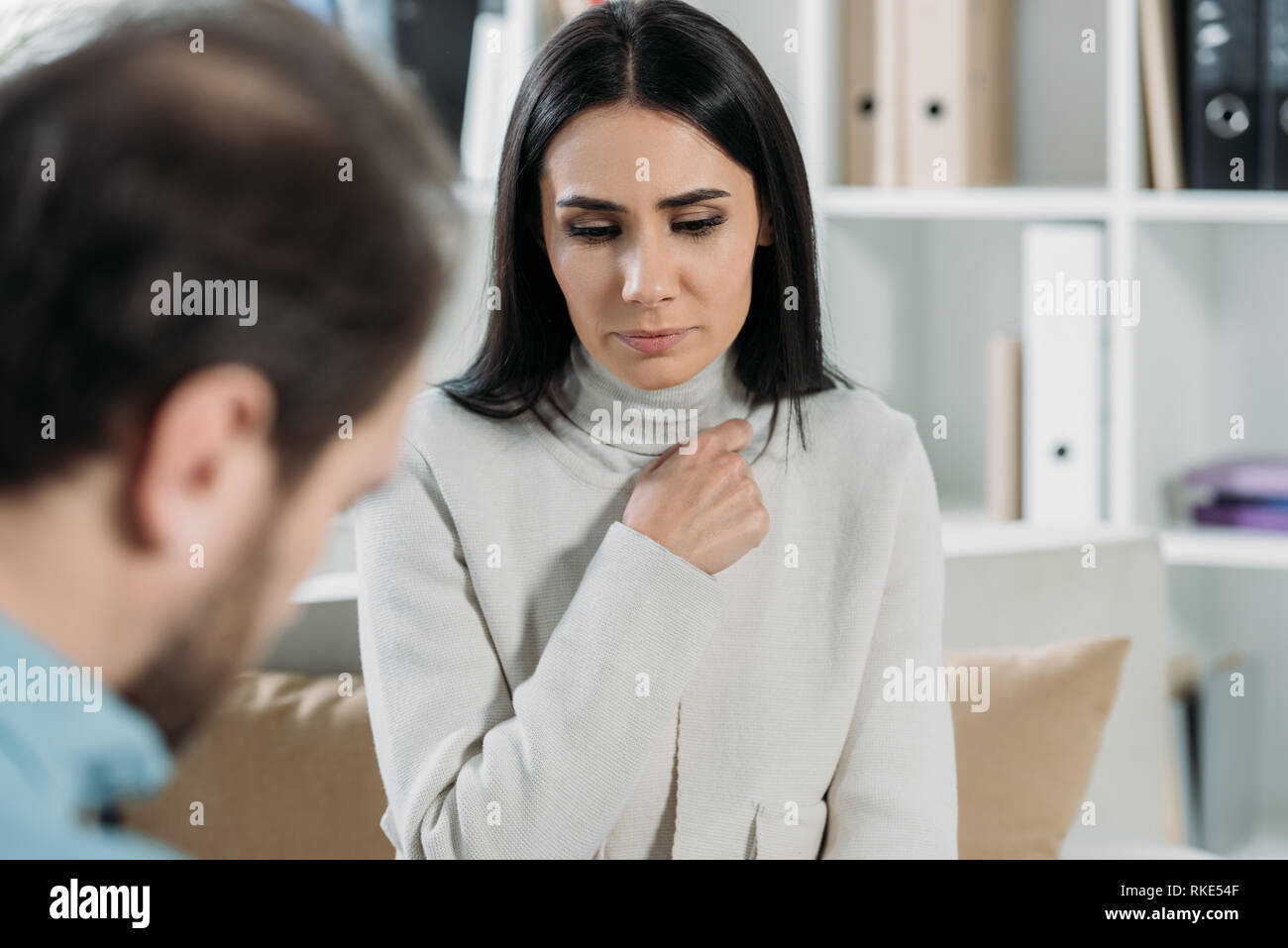 selective focus of unhappy young patient looking down while talking with psychotherapist in office Stock Photo