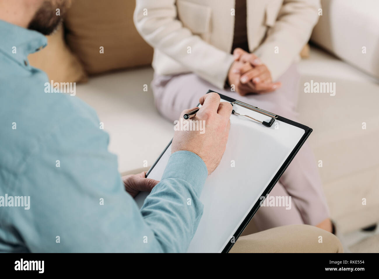 cropped shot of psychotherapist writing on clipboard and female patient sitting on couch Stock Photo