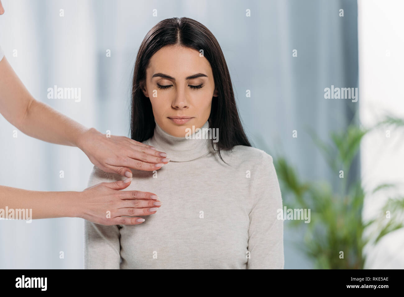 cropped shot of peaceful young woman with closed eyes sitting and receiving reiki treatment Stock Photo