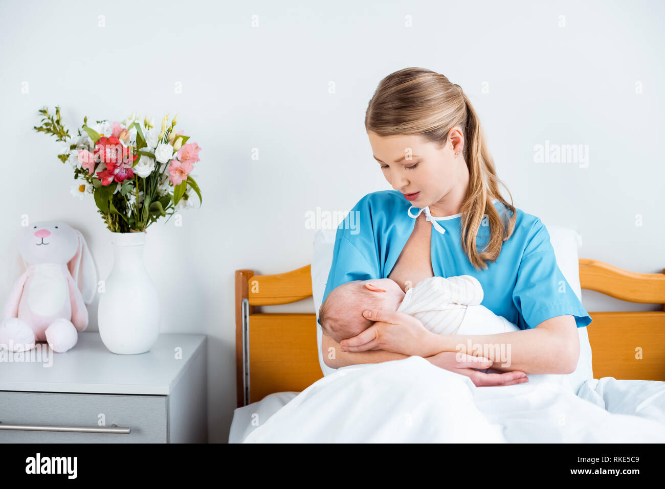 young mother sitting in bed and breastfeeding newborn baby in hospital