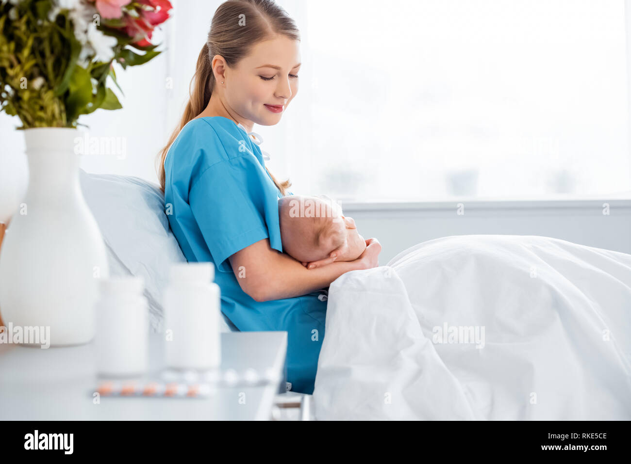 side view of happy young mother sitting on bed and breastfeeding