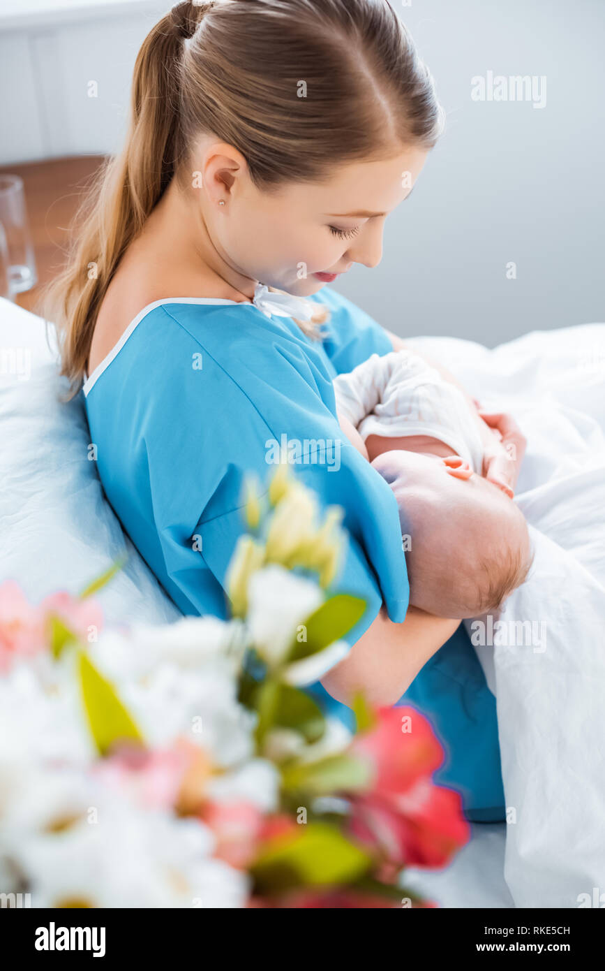 side view of smiling young mother breastfeeding newborn baby on bed in
