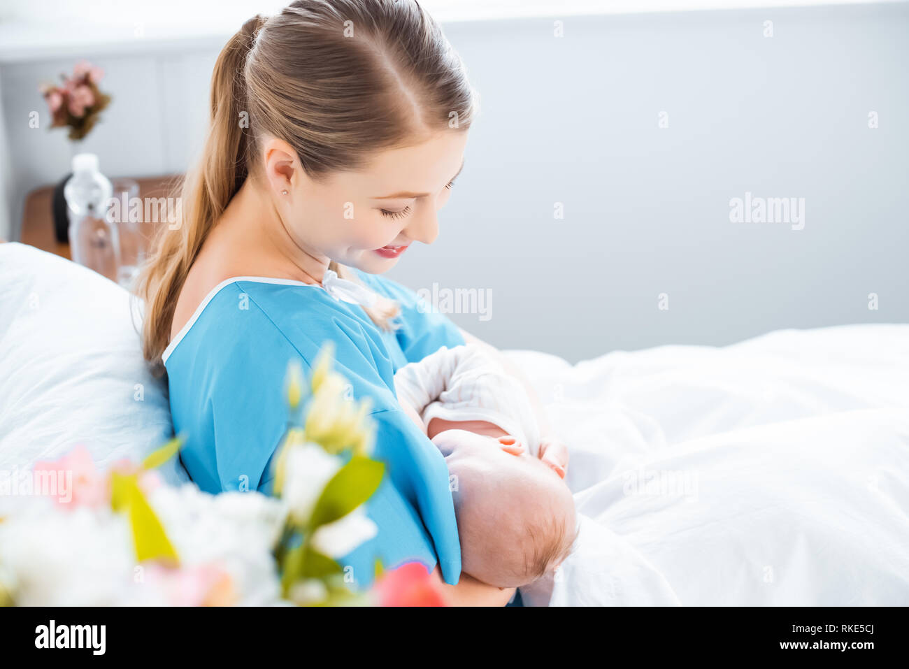 side view of happy young mother breastfeeding newborn baby on bed in