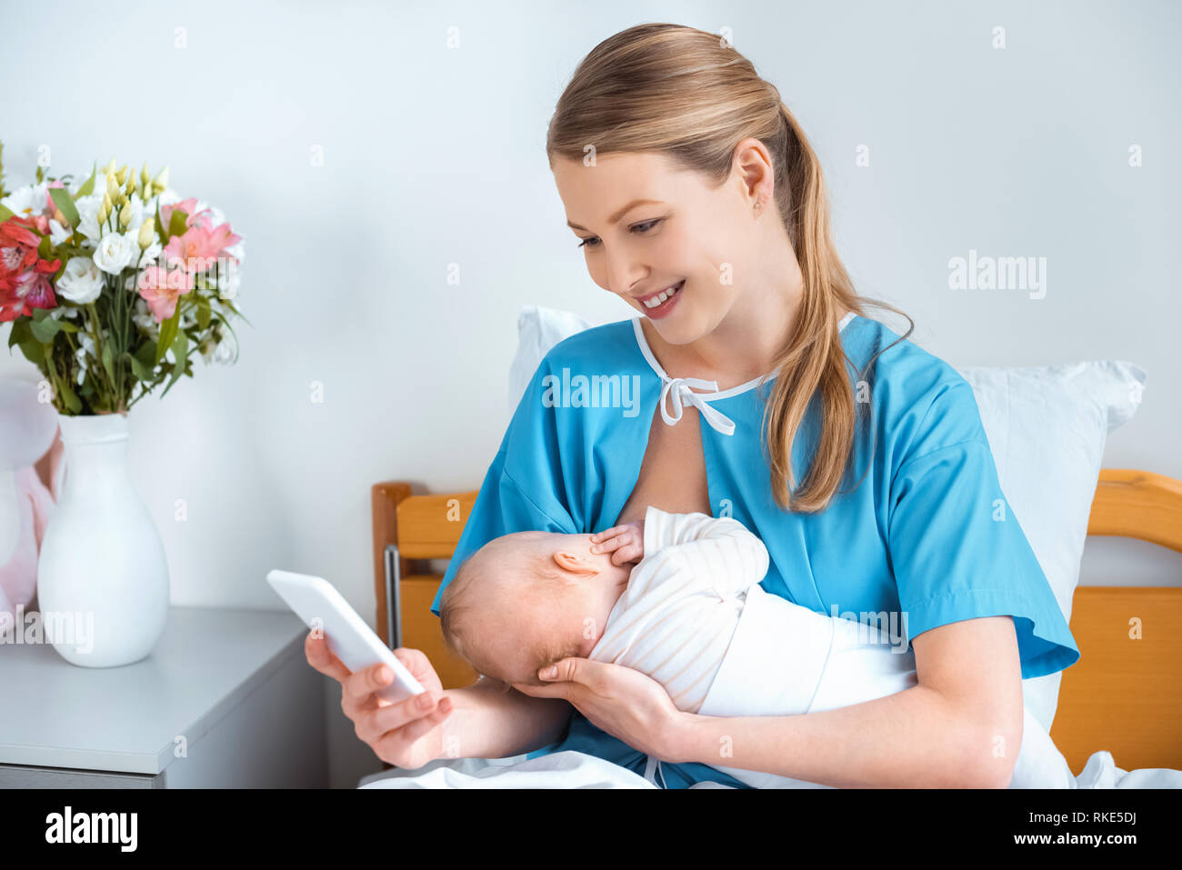 beautiful smiling young mother breastfeeding baby and using smartphone