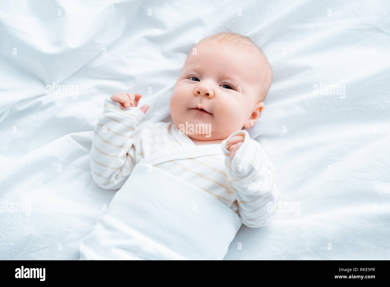 top view of adorable baby looking at camera while lying on white bedding Stock Photo