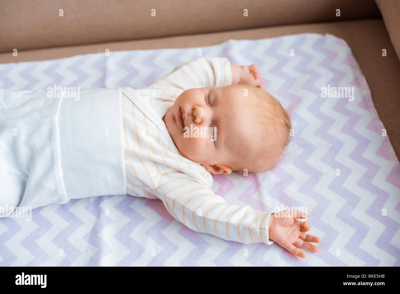 adorable newborn baby with closed eyes and raised hands lying on sofa Stock Photo