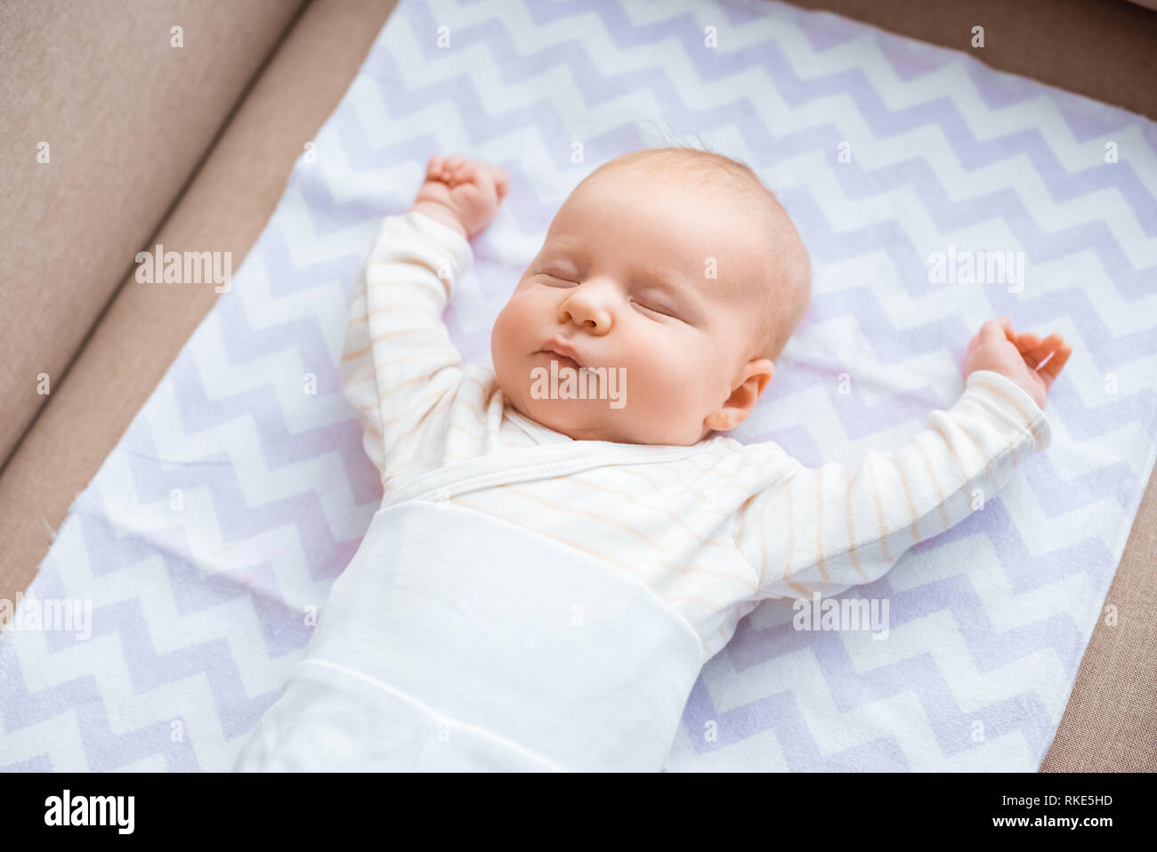 adorable baby with closed eyes and raised hands lying on couch Stock Photo