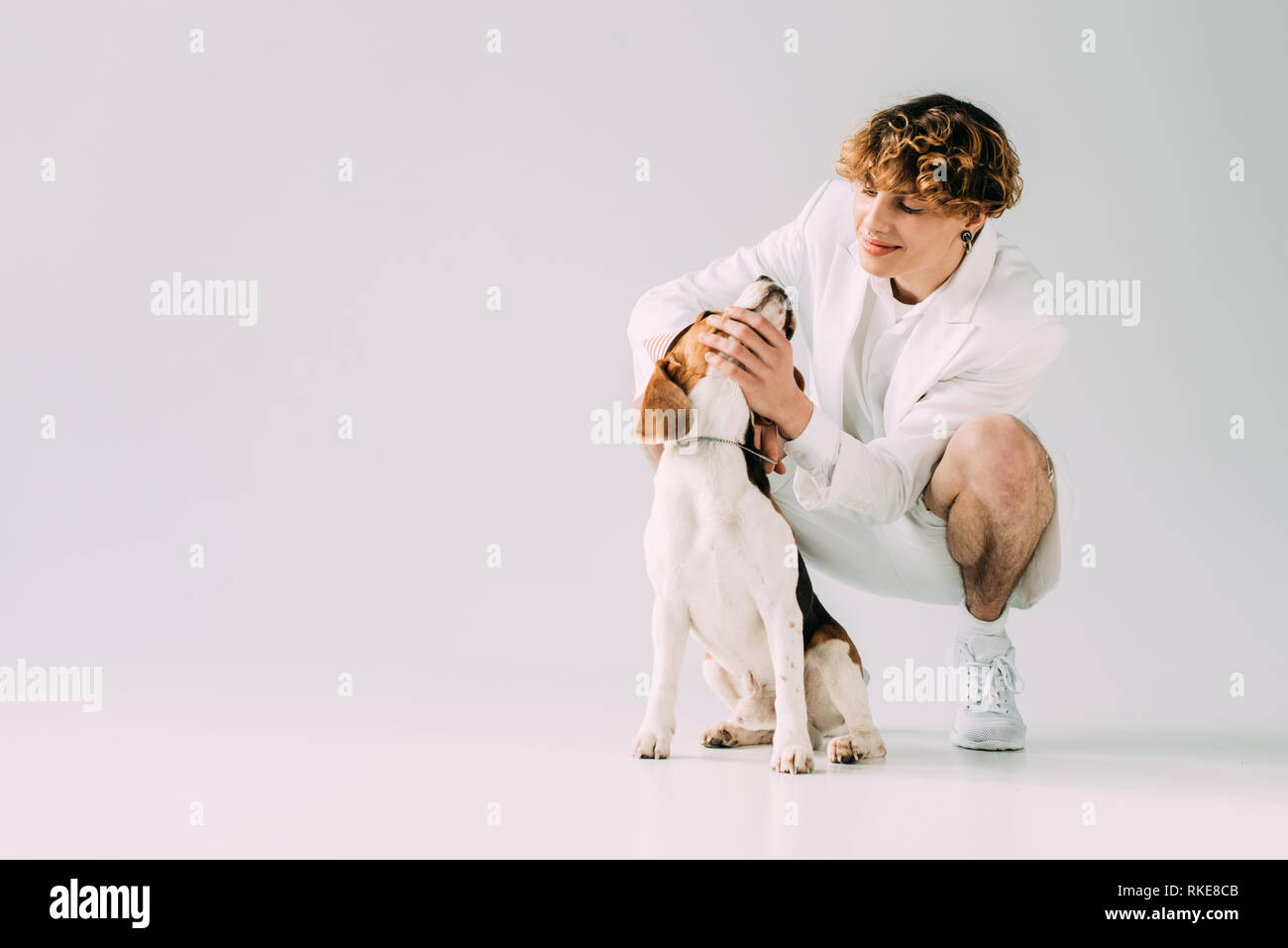 Happy Man With Curly Hair Looking At Beagle Dog On Grey