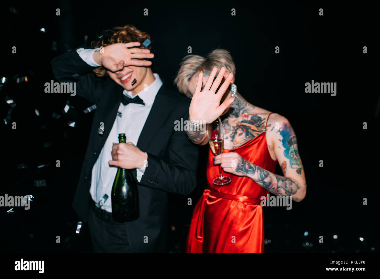 couple covering face while holding alcohol drinks on party isolated on black Stock Photo